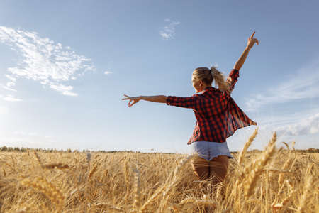 Silhouettes of a slender young woman with outstretched arms. A woman stands in a field of golden wheat. The atmosphere is summer and joyful. High quality photoの写真素材