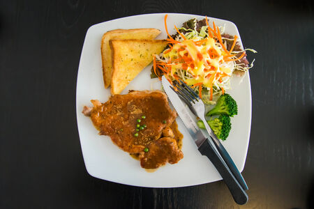 Pork steak with toast on a wooden table.