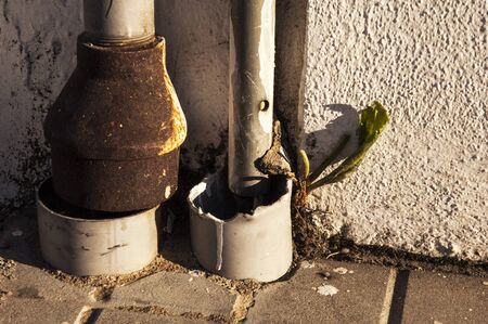 Water drains from a roof down to the ground old rusty and bungling together with sunset lightの写真素材