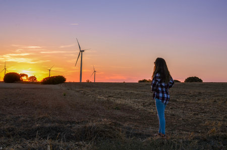 Woman in a sustainable field watching the sunset, surrounded by energy mills.の写真素材