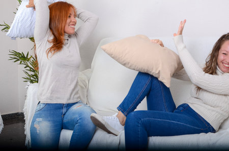 two sisters having a pillow fight on the couch at home one afternoon