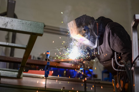 worker welding iron with electric welding equipment in the workshop, with protective equipment