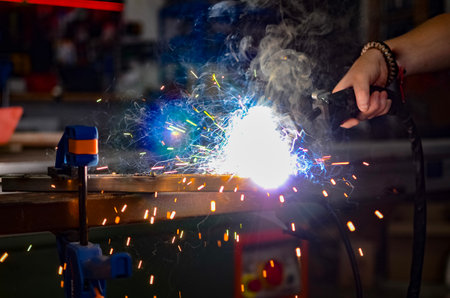 worker welding iron with electric welding equipment in the workshop, with protective equipment