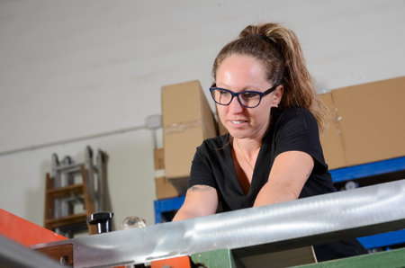 Female carpenter cutting wood in her workshop, dressed in black work clothes and protective glasses
