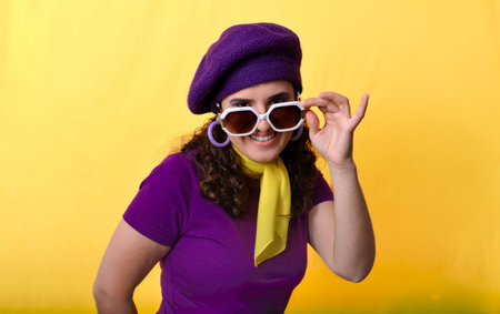 Studio portrait of a stylish woman adjusting her sunglasses and smiling