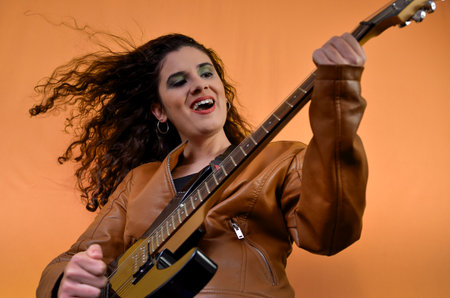 Musician expressing herself through music, playing electric guitar with energy and passion in studio...