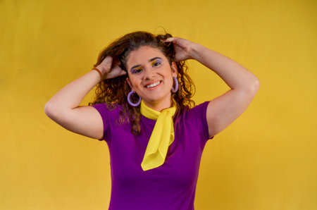 Studio portrait of a cheerful young woman holding her curly hair, smiling, wearing a purple t-shirt and yellow scarfの写真素材