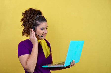 Young woman wearing headset and holding laptop while working as telemarketer or customer support...