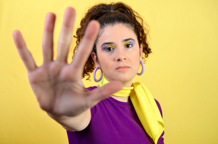 Serious woman showing stop sign with hand, expressing denial or rejection, on a yellow background