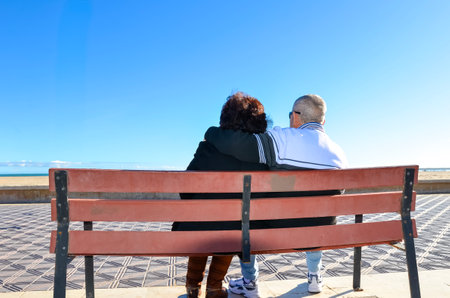 Senior couple enjoying peaceful moment on bench, embracing and taking in serene ocean viewの写真素材