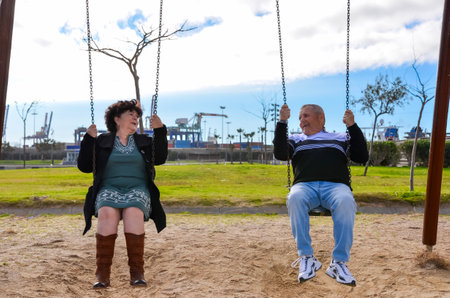 Elderly couple having fun swinging in a park, enjoying their retirement and leisure time togetherの写真素材