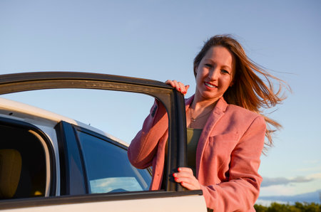 Smiling businesswoman getting out of her car during a road trip at sunsetの写真素材