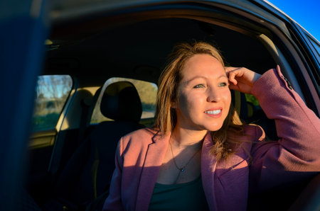 Businesswoman looking out of car window, enjoying sunset view during road tripの写真素材