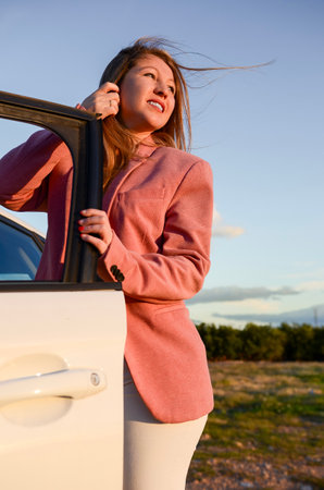 Young businesswoman getting out of car, enjoying the sunset during a relaxing car trip in the countrysideの写真素材