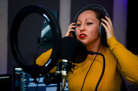 Young woman recording audio track in professional studio, wearing headphones and singing into microphoneの写真素材