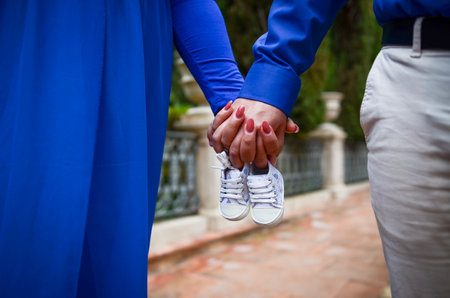 Happy couple holding hands and baby shoes, excited for their upcoming parenthoodの写真素材