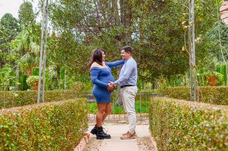 Happy pregnant couple embracing in a park, enjoying a tender moment together surrounded by natureの写真素材
