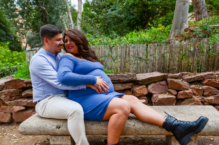 Pregnant woman and her husband sitting on a bench in a park, enjoying the anticipation of their babyの写真素材