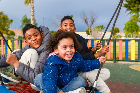 Three siblings enjoying a playful moment together on a swing in a playgroundの写真素材