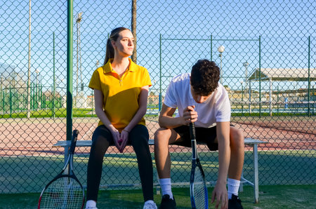 Two tennis players are sitting on a bench, resting after a tennis training sessionの写真素材