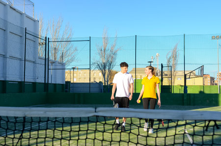 Two tennis players are walking off the court after a match, discussing the game and holding their racketsの写真素材