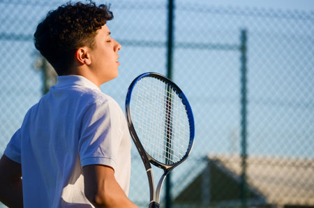 Young tennis player holding racket and breathing on court after matchの写真素材