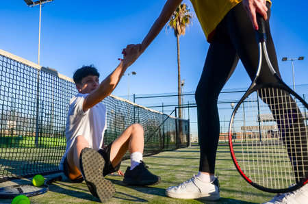 Sportsman helping his opponent to get up from the ground on a tennis courtの写真素材