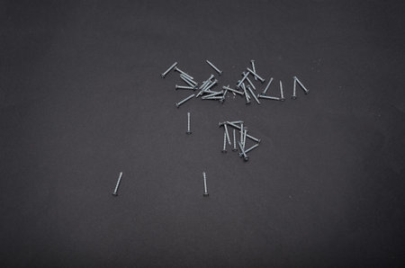 Small metal screws scattered randomly on a black background