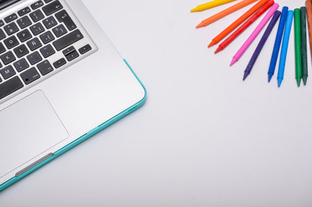 Laptop and crayons forming a colorful and vibrant back to school concept on a white backgroundの写真素材