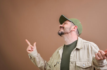 Technician pointing with his index finger to the top right corner, smiling and wearing a cap and a jacketの写真素材