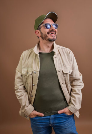 Studio portrait of a smiling man wearing sunglasses and a cap, looking upwards with hands in pocketsの写真素材