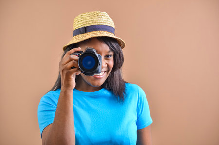 Happy photographer smiling and taking photos with professional digital camera in studio with brown backgroundの写真素材