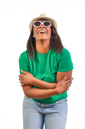 Studio portrait of a cheerful black woman laughing and hugging herself, wearing sunglasses and a hat, isolated on a white backgroundの写真素材