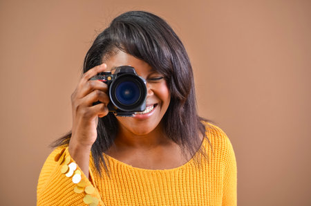 Happy photographer taking pictures with professional camera in studio with brown backgroundの写真素材