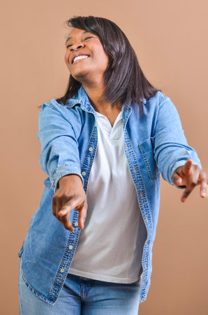 Happy woman wearing denim shirt pointing her fingers while smiling and looking up against brown backgroundの写真素材