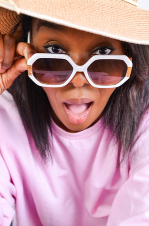 Studio portrait of a surprised model lowering her sunglasses and wearing a summer hatの写真素材