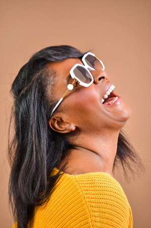 Studio portrait of a cheerful black woman wearing stylish sunglasses, laughing with her head tilted backの写真素材