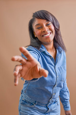 Young woman wearing denim shirt and jeans extending hand with a friendly smile, offering help and supportの写真素材