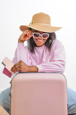 Young black woman with sun hat and sunglasses holding passport and smartphone is ready for summer vacationの写真素材