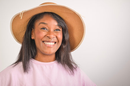 Studio portrait of a cheerful young woman wearing a sun hat and a pink shirt, expressing happiness and confidenceの写真素材