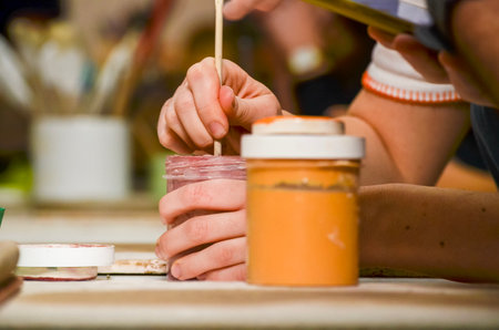 Potter mixing ceramic glaze in a jar using wooden stick, preparing for painting pottery