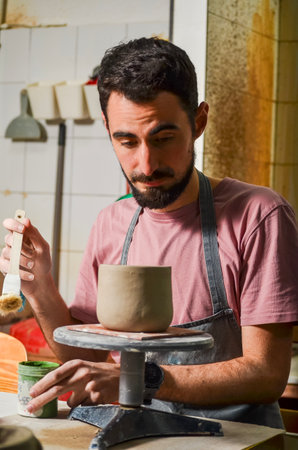 Concentrated craftsman painting a clay pot in his workshop using a brushの写真素材