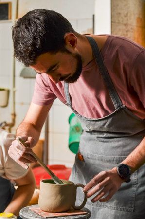 Concentrated craftsman painting a clay mug with green paint in his pottery workshopの写真素材