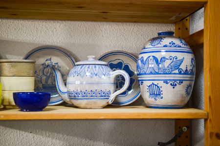 Beautiful hand-painted pottery, including a teapot, plates, a vase, and a bowl, sits on a wooden shelf, showcasing traditional craftsmanshipの写真素材