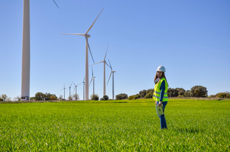 Engineer holding tablet, inspecting wind turbines in a green field, working on renewable energy and sustainabilityの写真素材