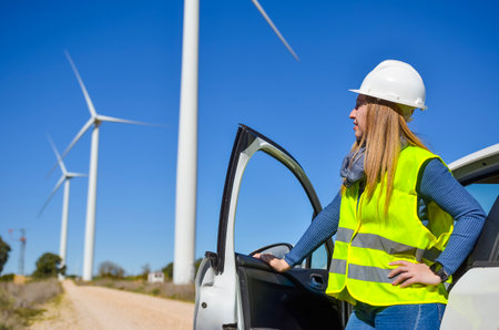 Engineer exiting his car and looking at wind turbines in a wind farm, working on renewable energy productionの写真素材