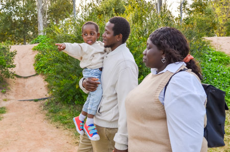 Smiling african american family enjoying a walk in the park, with their child pointing at something in the distanceの写真素材