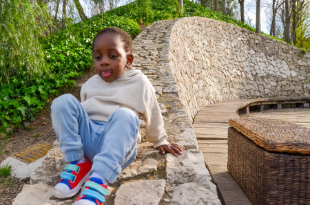 Young child sits on a low stone wall in a park, enjoying the peaceful surroundingsの写真素材