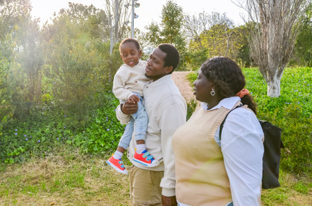 Smiling african parents holding their child walking in park enjoying sunny dayの写真素材