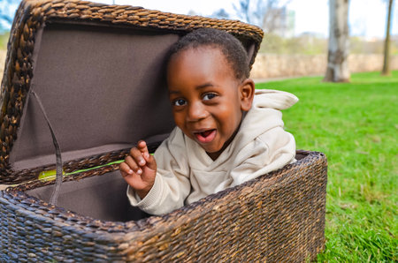 Smiling black child having fun sitting inside wicker basket in parkの写真素材